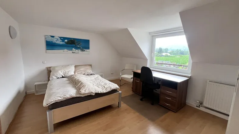 Helles Schlafzimmer im Dachgeschoss mit Holzboden, Schreibtisch und Blick ins Grüne.