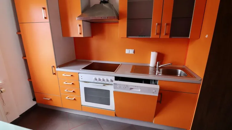 Kleine Küche mit leuchtend orangefarbenen Schränken, integrierten Geräten und Dunstabzugshaube.