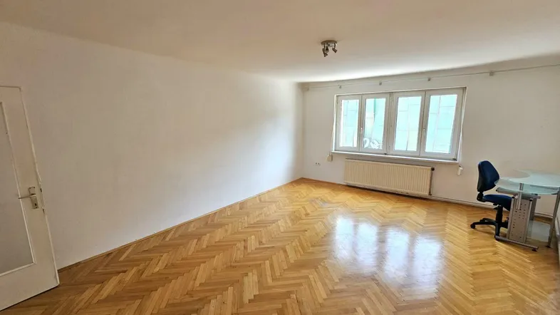 Helles Wohnzimmer mit Fischgrätparkettboden und einem kleinen Schreibtischbereich am Fenster.