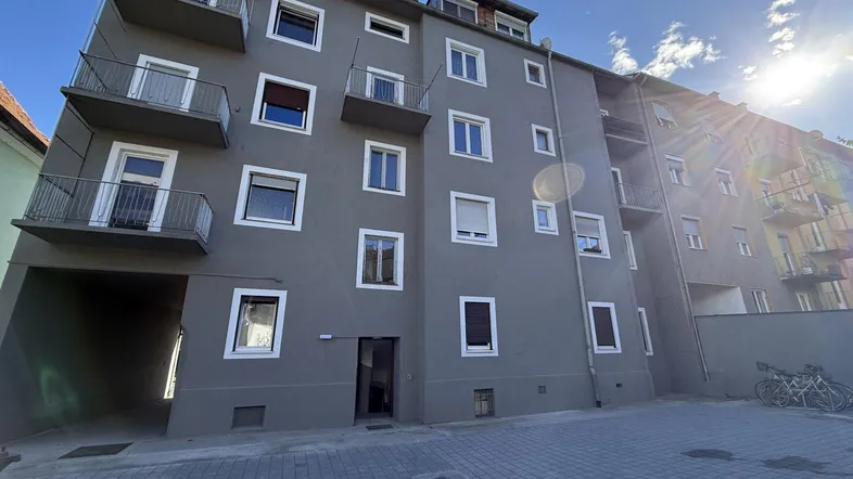 Modernes Mehrfamilienhaus mit grauer Fassade, weißen Fenstern und kleinen Balkonen.