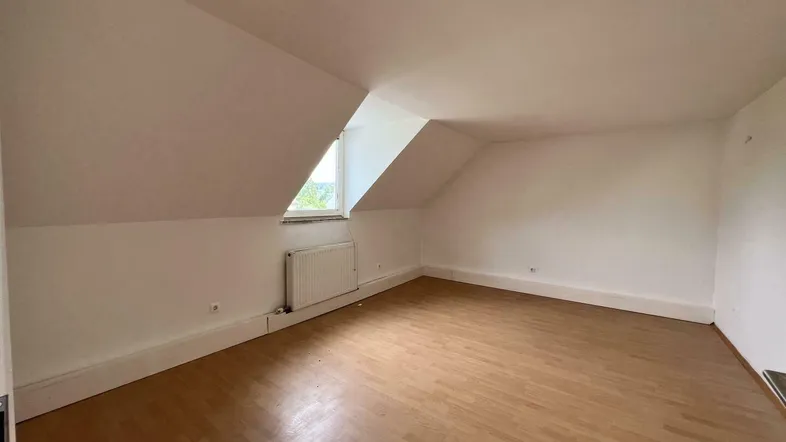 Helles Zimmer im Dachgeschoss mit Laminatboden und schrägen Wänden, bereit zur individuellen Gestaltung.