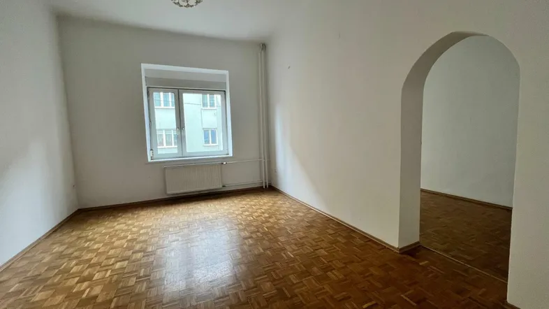 Helles Zimmer mit Fischgrätparkettboden, weißen Wänden und einem Fenster mit Blick nach draußen.