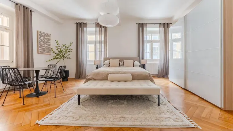 Helles Schlafzimmer mit Parkettboden, großem Bett, Einbauschränken und einem kleinen Essbereich.