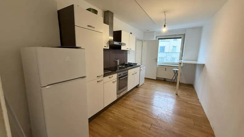 Helle Küche mit weißen Schränken, Holzparkettboden und einem Fenster mit Blick nach draußen.
