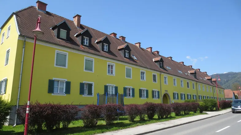 Lange gelbe Fassade eines Gebäudes mit roten Dächern und vielen Dachgauben entlang einer Straße.