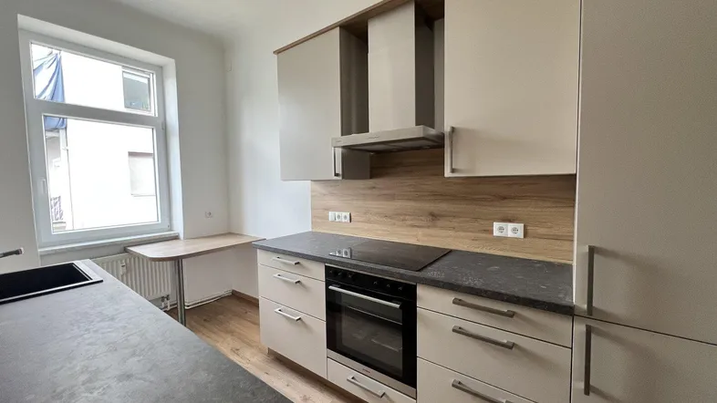 Moderne Küche mit hellen Schränken, dunkler Arbeitsplatte, Induktionskochfeld und integriertem Backofen.