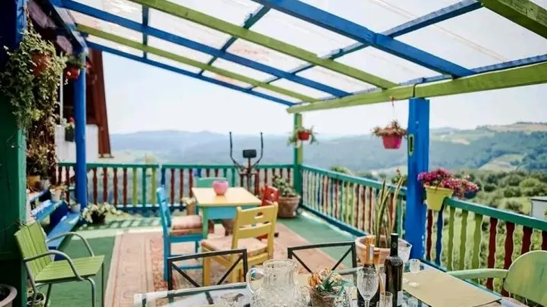 Bunte überdachte Terrasse mit Esstisch und Stühlen, bietet einen weiten Blick auf die Landschaft.