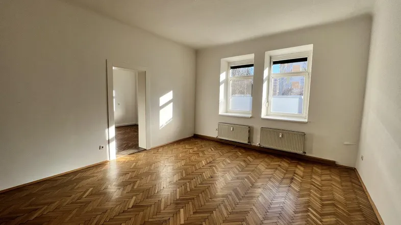 Helles, leeres Zimmer mit Fischgrätparkettboden und zwei Fenstern, bereit zur individuellen Gestaltung.