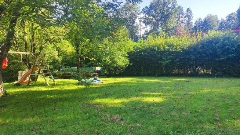 Großer, sonniger Gartenbereich mit Rasenfläche, Spielgeräten und umgebenden Bäumen und Hecken.