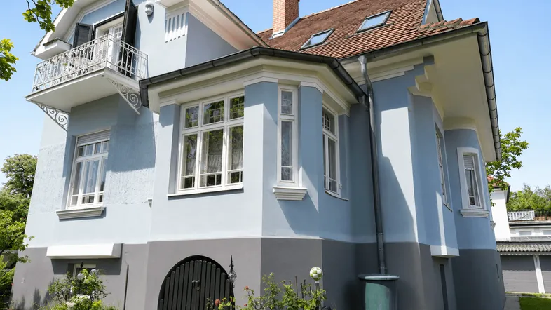 Historisches Haus mit hellblauer Fassade, roten Ziegeln und kleinem Balkon.