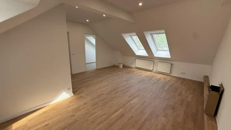 Geräumiger Dachgeschossraum mit Holzboden, Dachfenstern und viel natürlichem Licht.