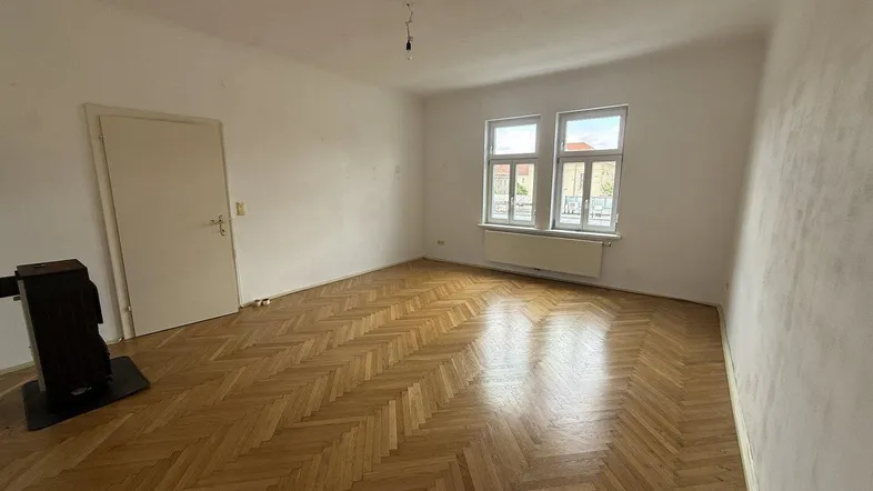 Helles Zimmer mit Fischgrätparkett, weißen Wänden und einem Holzofen, bereit zur individuellen Gestaltung.
