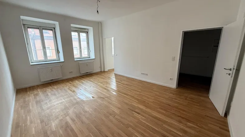 Helles Zimmer mit Holzboden und zwei Fenstern, bereit zur individuellen Gestaltung.
