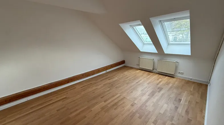 Helles Dachzimmer mit Holzbalken, zwei Dachfenstern und Parkettboden, ideal als Schlaf- oder Arbeitszimmer.