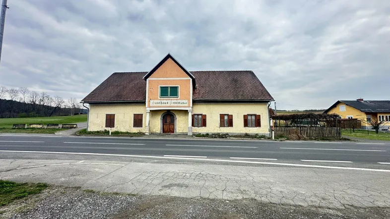 Altes Gasthausgebäude an einer Landstraße in ländlicher Umgebung mit braunen Fensterläden.