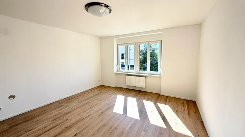 Freundliches Zimmer mit Laminatboden, großen Fenstern und viel Tageslicht.