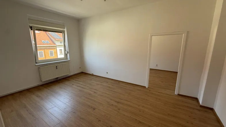 Helles, leeres Zimmer mit Laminatboden und weiß gestrichenen Wänden, bereit zur individuellen Gestaltung.