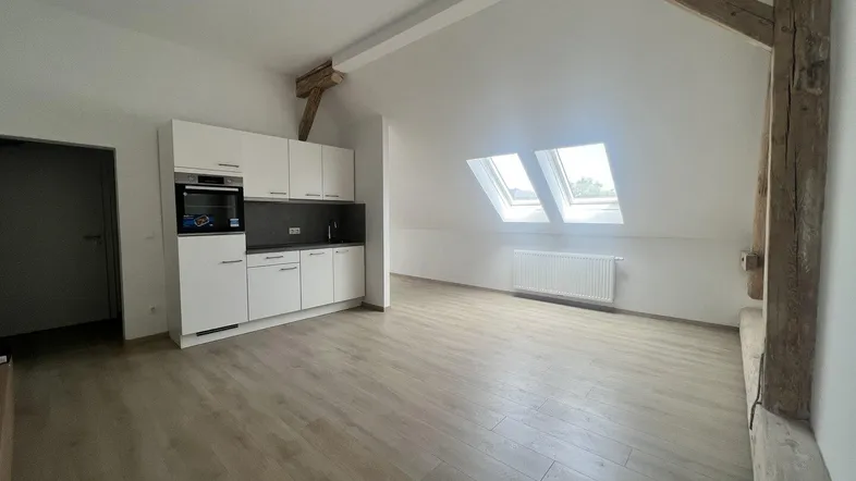 Helles Dachgeschosszimmer mit integrierter Küchenzeile, Holzbalken und Dachfenstern.