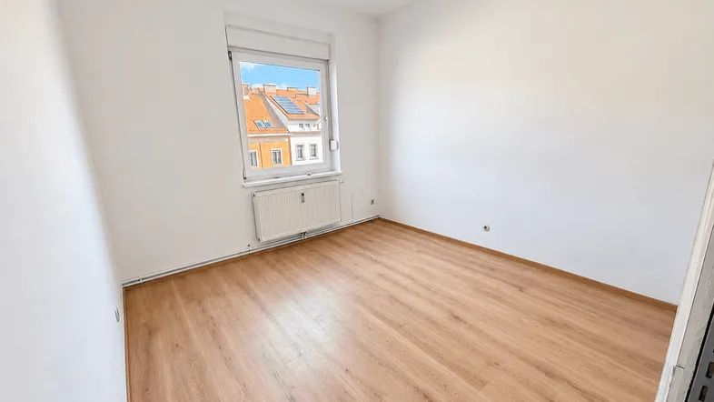Helles, leeres Zimmer mit Laminatboden und Blick auf die umliegenden Dächer.