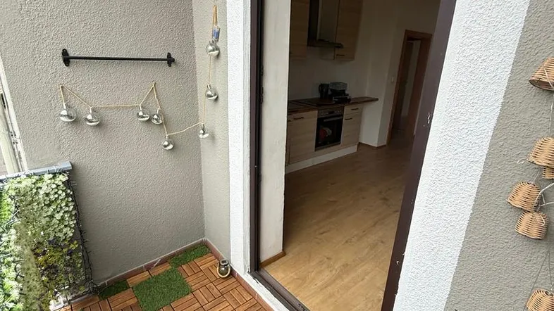 Kleiner Balkon mit Holzbodenfliesen und künstlichem Grün, der Zugang zur Küche bietet.