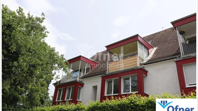 Fassade eines Mehrfamilienhauses mit roten Akzenten, Balkonen und viel Grün.