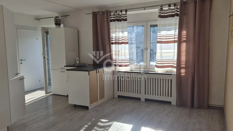 Helles Wohnzimmer mit integrierter Küchenzeile, großem Fenster und Vorhängen.