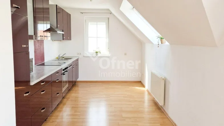 Helle Küche in Dachgeschosswohnung mit braunen Schränken, Arbeitsplatte und Holzfußboden.