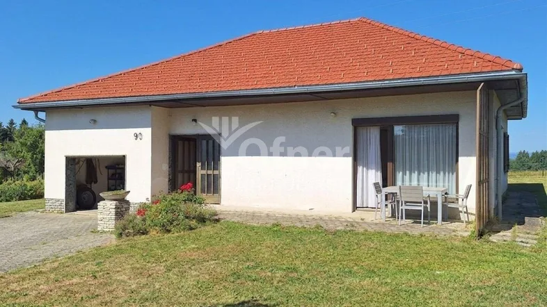 Einfamilienhaus mit rotem Ziegeldach, kleiner Terrasse und angrenzendem Gartenbereich.