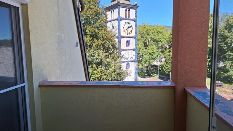 Kleiner Balkon mit Blick auf einen historischen Kirchturm und grüne Bäume in der Ferne.