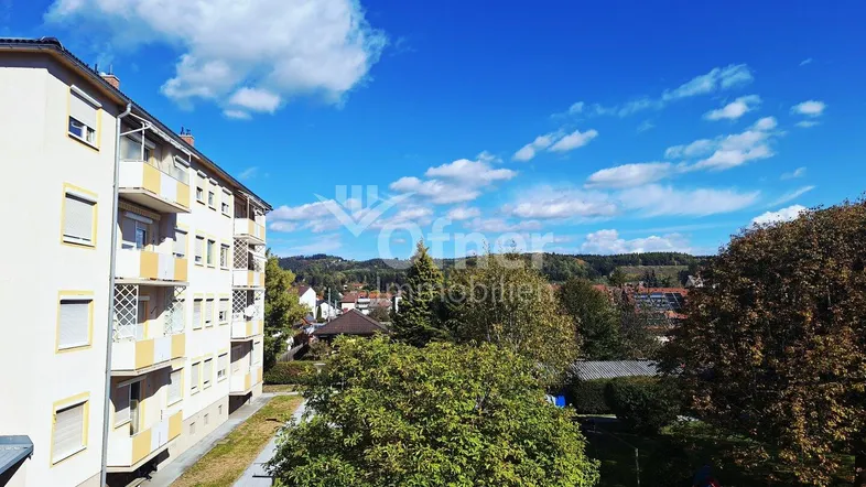 Apartmentgebäude mit Balkonen und Blick ins Grüne unter blauem Himmel.