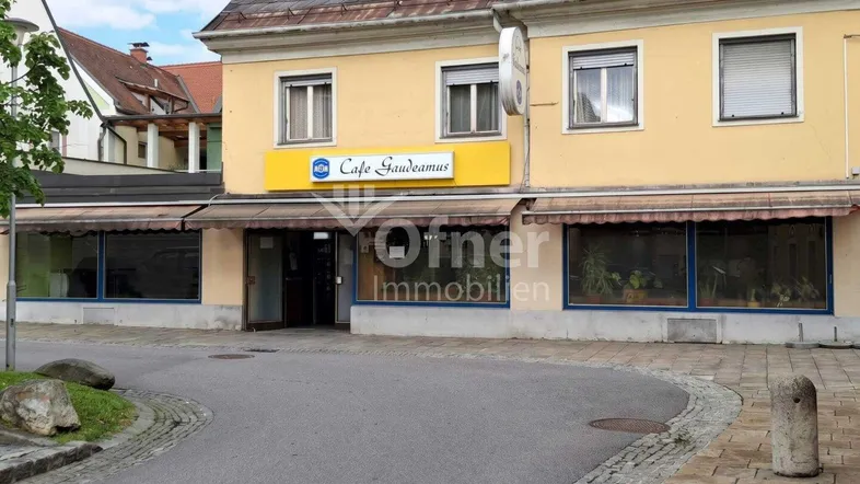 Gelbe Fassade eines Geschäftsgebäudes mit Markisen und Café-Beschilderung an einer Straße.
