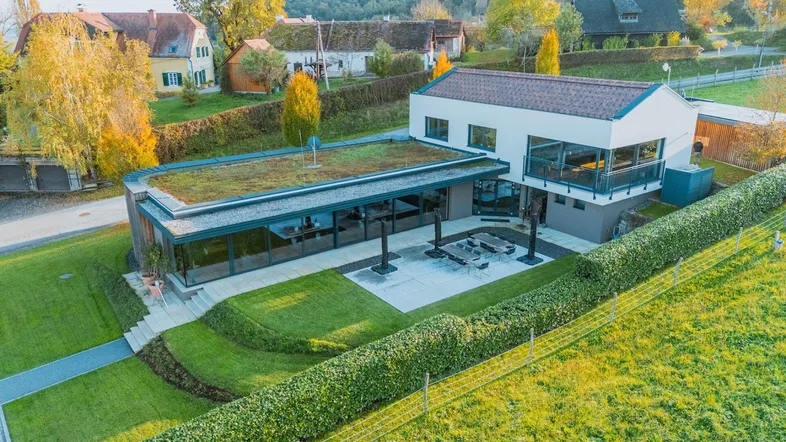 Modernes Gebäude mit Gründach, großer Terrasse und gepflegtem Garten in ländlicher Umgebung mit viel Grün.