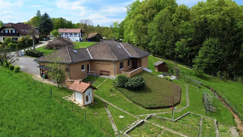 Luftaufnahme eines Einfamilienhauses mit großem Garten, umgeben von viel Grün und Bäumen.