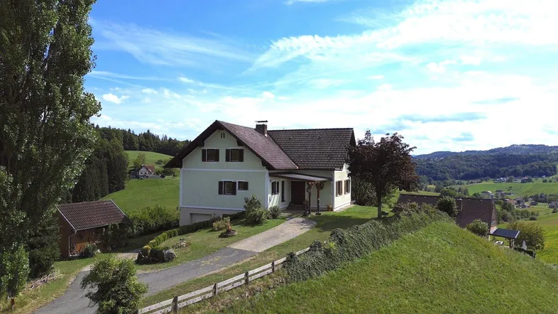Freistehendes Einfamilienhaus in ländlicher Umgebung mit grünen Hügeln und Bäumen unter blauem Himmel.