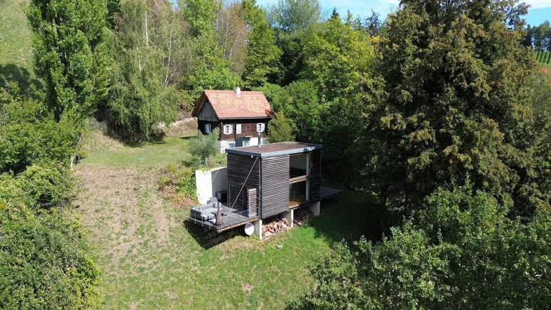 Luftaufnahme zweier Häuser in einer grünen, hügeligen Landschaft mit vielen Bäumen.