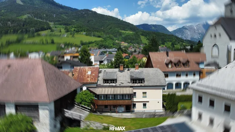 Luftaufnahme des Gebäudes in einer ländlichen Umgebung mit Bergen im Hintergrund und umliegender Bebauung.