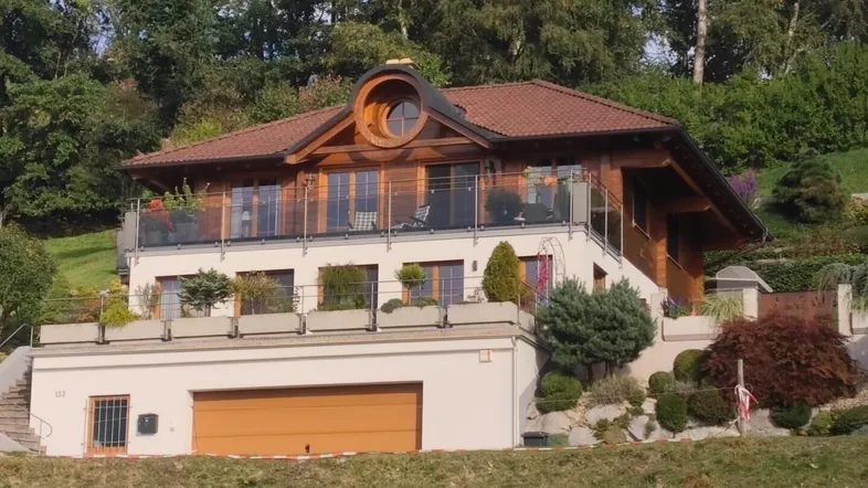 Charmantes Holzhaus mit mehreren Balkonen und integrierter Garage, eingebettet in eine grüne Hügellandschaft.