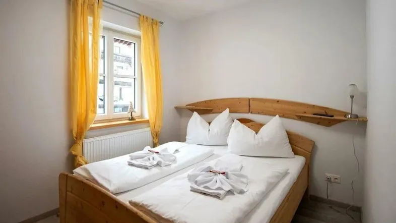 Gemütliches Schlafzimmer mit Doppelbett, Holzrahmen und gelben Vorhängen am Fenster.