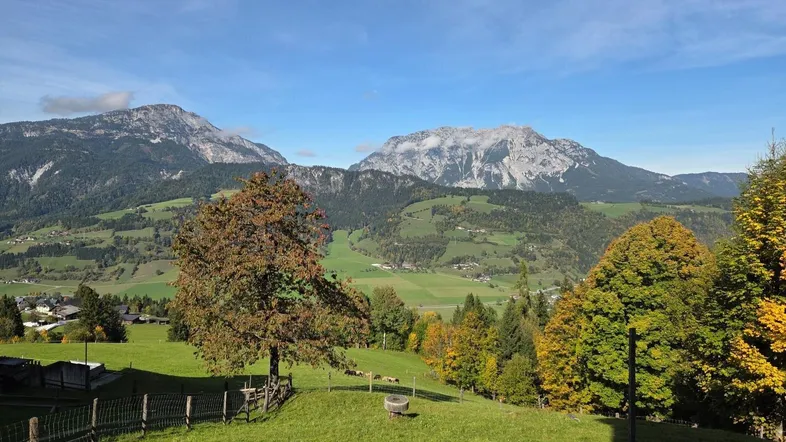 Malerische Berglandschaft mit grünen Wiesen und Bäumen unter blauem Himmel.