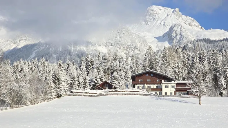 Großzügiges Anwesen in verschneiter Alpenlandschaft mit majestätischem Bergblick unter blauem Himmel.