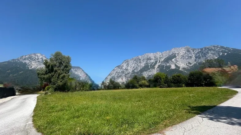 Weitläufige grüne Wiese mit beeindruckendem Bergblick unter klarem blauem Himmel.