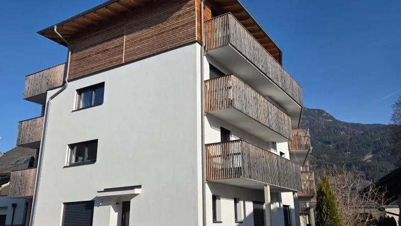 Modernes Mehrfamilienhaus mit Holzverkleidung und Balkonen unter blauem Himmel.