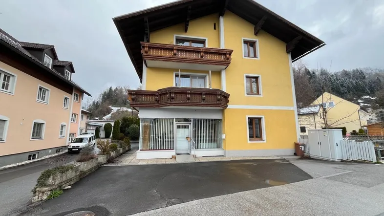 Gelbes Gebäude mit traditionellen Holzbalkonen und einem Ladenlokal im Erdgeschoss unter bewölktem Himmel.