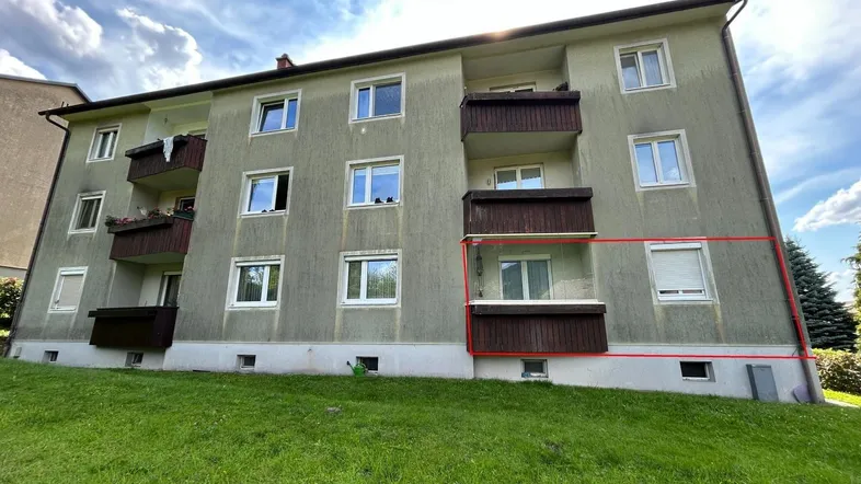 Mehrfamilienhaus mit mehreren Balkonen und einer grünen Rasenfläche davor unter blauem Himmel.