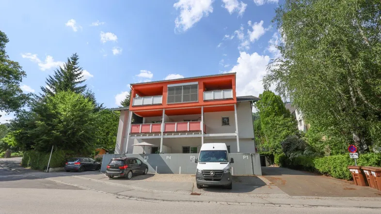 Modernes Mehrfamilienhaus mit leuchtend orangefarbenen Balkonen und Außenparkplätzen.