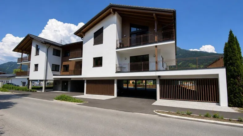 Modernes Mehrfamilienhaus mit Balkonen und Carports in alpiner Umgebung.
