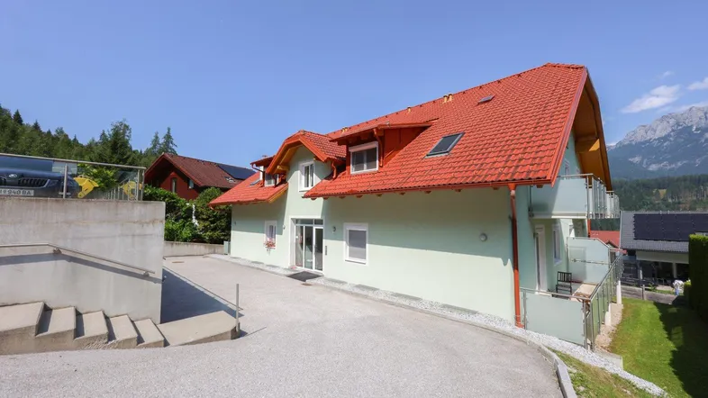 Modernes Wohnhaus mit rotem Ziegeldach und Zufahrt in bergiger Umgebung.