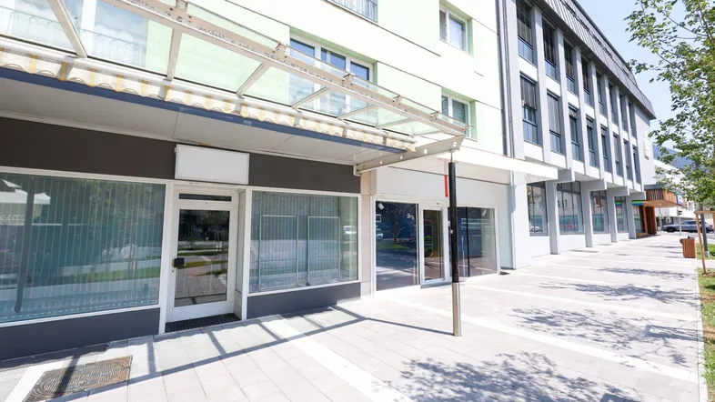 Moderne Geschäftsfassade mit großen Schaufenstern und einem Vordach an einem sonnigen Tag.