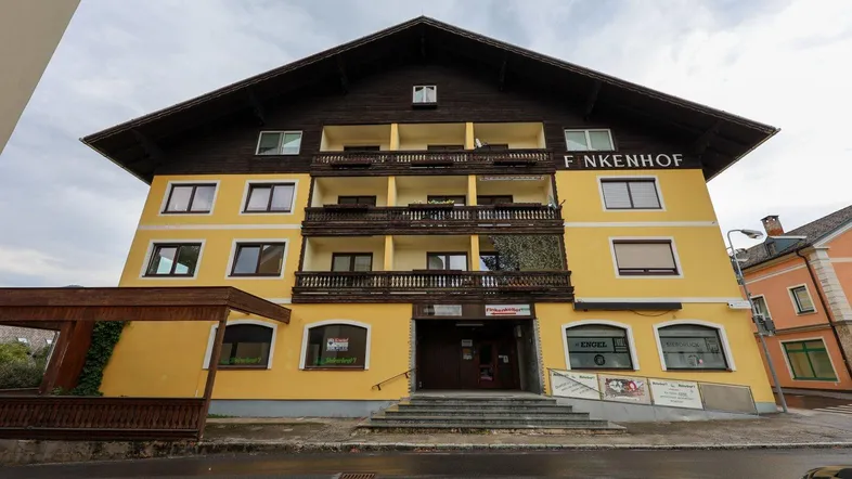 Gelbes Gebäude mit mehreren Balkonen und traditioneller Holzverkleidung unter dem Dach, gut gepflegt.