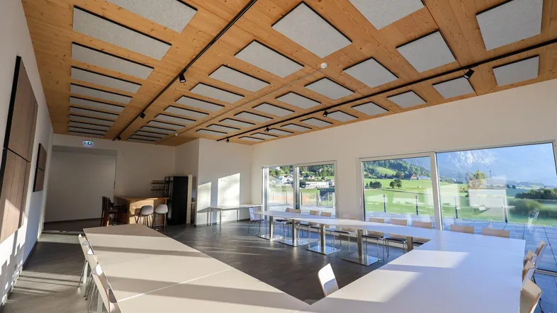 Großer, heller Konferenzraum mit Holzbalkendecke, Schallschutzplatten und großen Fenstern mit Bergblick.